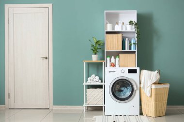 Çamaşır makinesi, raflar ve sepeti olan çamaşır odasının içi.