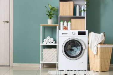 Çamaşır makinesi, raflar ve sepeti olan çamaşır odasının içi.