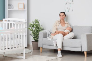 Küçük bebeğiyle yatak odasındaki kanepede oturan genç bir kadın. Tüp bebek konsepti