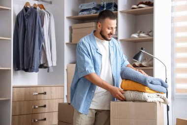 Soyunma odasında katlanmış süveter ve kıyafet kutularıyla genç bir adam.