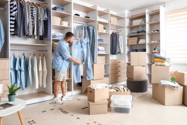 Soyunma odasında kot pantolon ve kostüm kutularıyla genç bir adam.