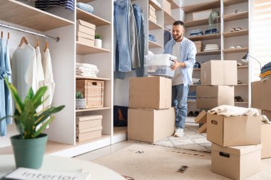 Genç adam soyunma odasındaki dolaplara ayakkabılı konteynırlar koyuyor.