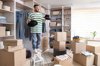 Soyunma odasında şapkalı, kostüm kutusu olan genç bir adam.