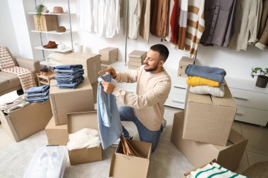 Giysi kutularıyla genç adam soyunma odasında gömleğini askıya asıyor.