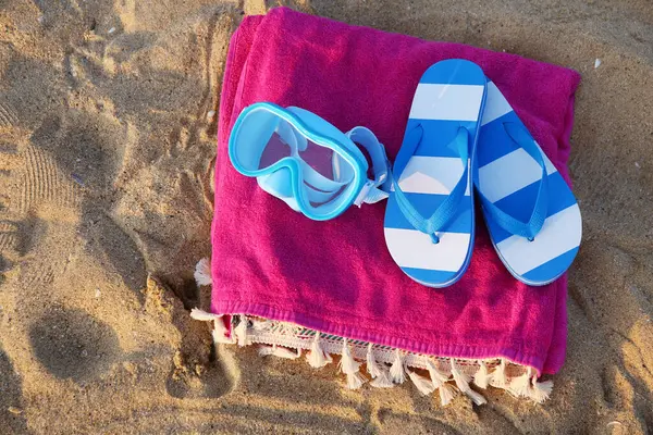 Şnorkelli maske, parmak arası terlikler ve deniz sahilinde renkli bir havlu.