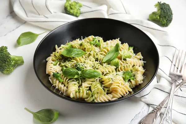 Siyah kase lezzetli fusilli makarna brokoli ve fesleğen yapraklı beyaz arka plan, yakın plan.