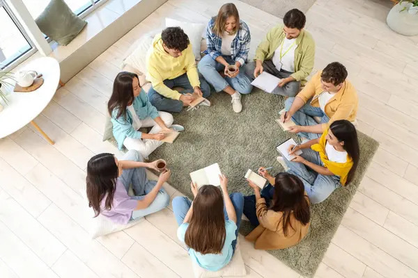 Gençler grup terapi seansında halıya not defterleri yazıyorlar.