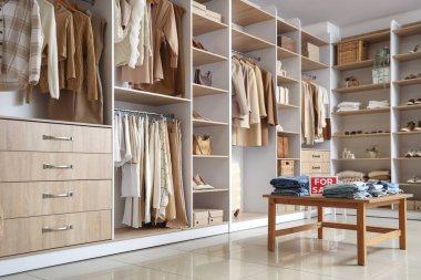 Rafları, masası ve şık kıyafetleri olan bir butiğin içi.