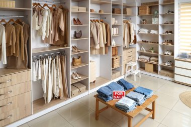 Rafları, masası ve şık kıyafetleri olan bir butiğin içi.