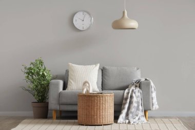Oturma odasının içinde duvar saati, gri kanepe ve sepet var.