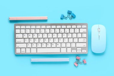 Gri klavye, bilgisayar faresi ve mavi arka planda kırtasiye malzemesi. Üst görünüm