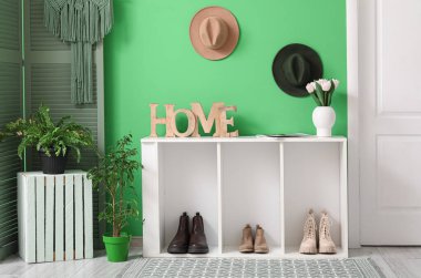 Güzel bir salonun içinde raf ünitesi, çiçek buketi ve yeşil duvarın yanındaki bitki örtüsü.