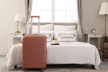 Otel odasının içinde, yatağın yanında bavul var.