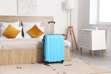 Otel odasının içinde, yatağın yanında bavul var.