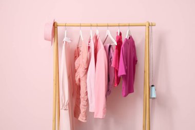 Rack with female clothes near pink wall