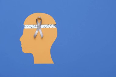 Beyni ve mavi arka planda gri farkındalık kurdelesi olan kağıt insan kafası. Kanser kavramı