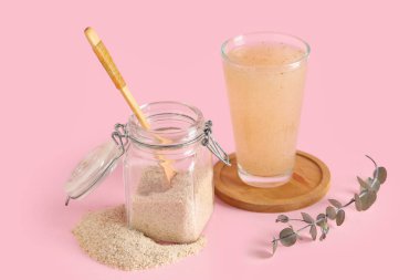 Psyllium kabuklu kavanoz ve pembe arka planda bir bardak su.