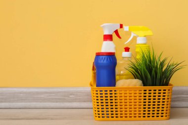 Sarı duvarın yanında temizlik malzemeleri olan sepet.