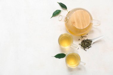 Bardaklar ve çaydanlık, beyaz arka planda kurumuş yapraklı sıcak yeşil çay.