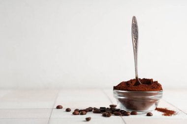 Bir kase kahve tozu, beyaz fayans üzerinde kaşık ve fasulye.