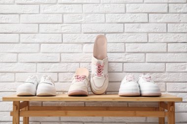 Beyaz tuğla duvarın yanındaki bankta ortopedik tabanlı spor ayakkabılar.