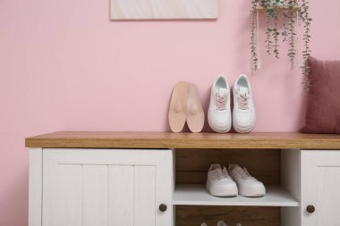 Koridordaki pembe duvarın yanındaki bankta ortopedik tabanlı spor ayakkabılar.