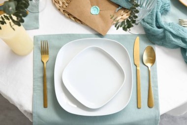 Restoranda temiz tabaklar ve altın çatal bıçak takımı olan şık bir masa.