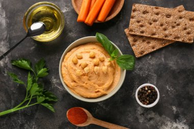 Siyah grunge arka planında havuç, nohut ve kraker olan lezzetli humus kasesi.
