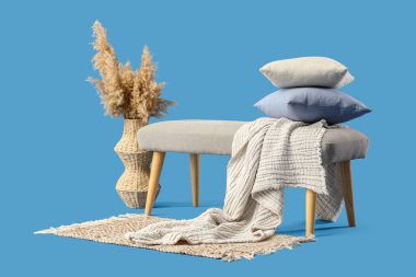 Mavi arka planda, yastıklı, ekoseli ve otlu bir vazo.