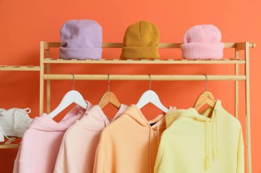 Turuncu duvarın yanında kapüşonlu ve şapkalı raflar