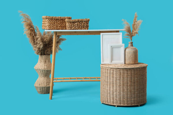 Wooden stand with wicker baskets and pampas grass in vases on blue background