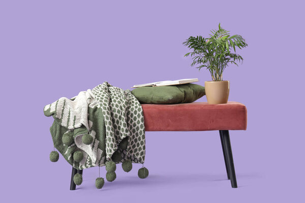 Pink bench with book, pillow, plaid and plant on lilac background
