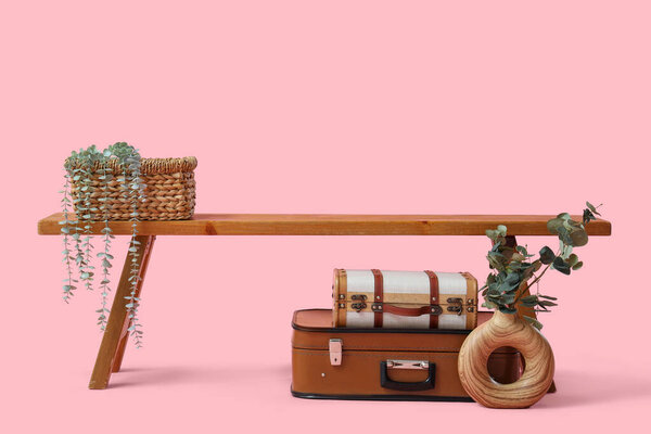 Wooden bench with plants and retro suitcases on pink background