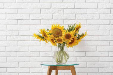 Kahve masasının üstünde vazo ve beyaz tuğla duvarın yanında.