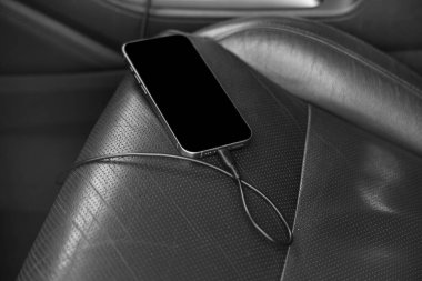 Arabada koltukta şarj kablosu olan cep telefonu, yakın plan.
