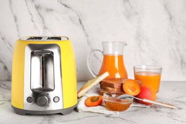 Beyaz mermer arka planda ekmek dilimleri, kayısılar ve reçel ile sarı tost makinesi