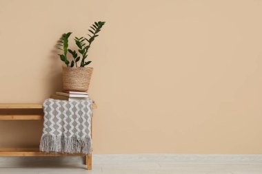 Odadaki bej duvarın yanındaki bankta saksı, kitap ve ekose.