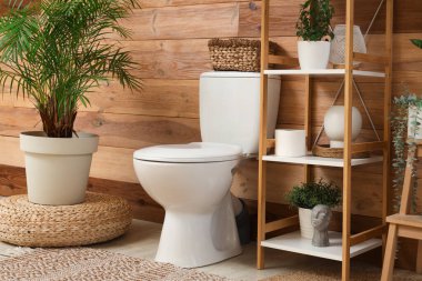 Tuvaletin içinde seramik klozet, raf ünitesi ve bitkiler var.