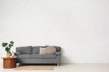 Rahat kanepesi, sehpası ve beyaz tuğla duvarın yanındaki bitki örtüsü olan şık bir oturma odası.