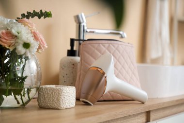 Kozmetik çantalı modern fotoepilatör, mum ve çiçekler banyoda lavabonun yanındaki masada.