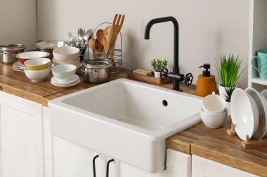 Seramik lavabo, temiz tabaklar ve mutfak aletleri ahşap tezgahta.