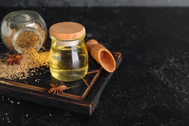 Ahşap tahta tahta, gerekli yağ şişesi, anason yıldızları, kurutulmuş tohumlar ve siyah grunge arka planda kepçe