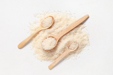 Beyaz arka planda çiğ pirinçli tahta kaşıklar.