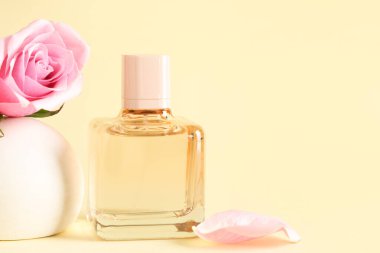 Bir şişe parfüm ve sarı arka planda güzel güllü dekoratif podyum.