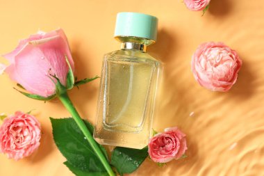 Bir şişe parfüm ve sarı arka planda suda güzel pembe güller.