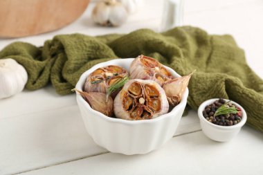 Beyaz ahşap arka planda fırında sarımsak, biberiye ve biberli mısır kasesi.