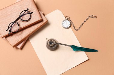 Kitaplı eski kağıt çarşaf, tükenmez kalem, mürekkep hokkası, gözlük ve bej arka planda cep saati.