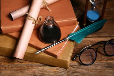 Ahşap arka planda kalem, mürekkep hokkası, parşömen ve gözlüklü eski kitaplar.