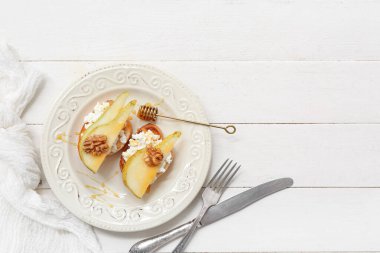 Beyaz ahşap zemin üzerinde ricotta peynirli ve cevizli armut bruschetta tabağı.