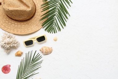 Yaz şapkalı güneş gözlükleri, deniz kabukları ve beyaz arka planda palmiye yaprakları.